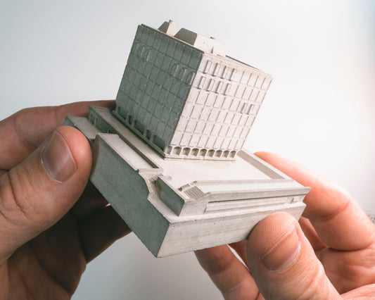 Hand holding a miniature model of a building against a light gray background